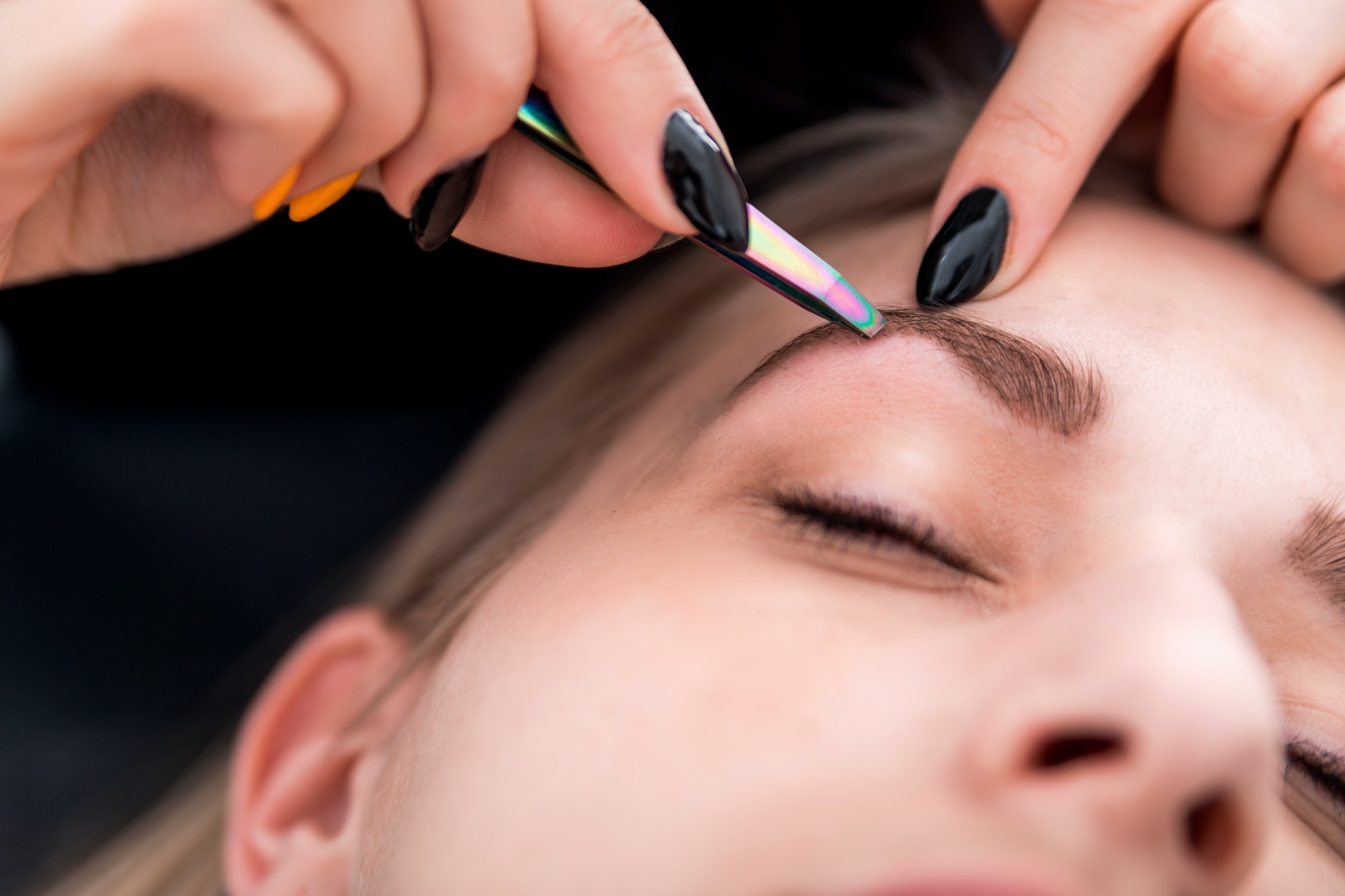 Plucking eyebrows with tweezer by beautician at beauty salon