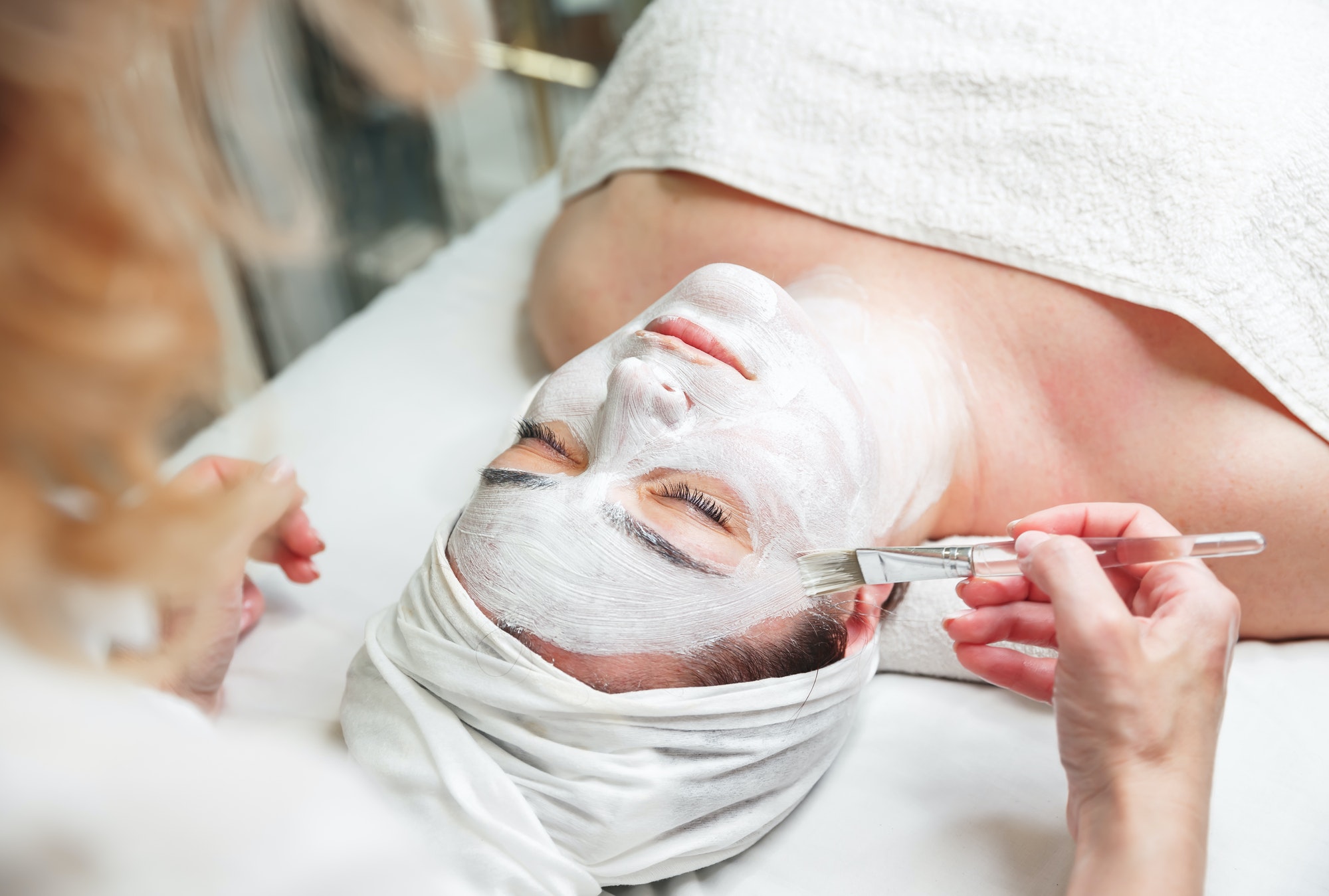 Woman get face mask by beautician at spa salon. Skin treatment concept